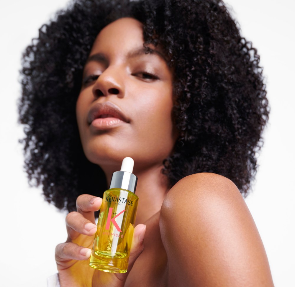 Ebonee Davis with her gorgeous curly hair holds the best hair oil for damaged hair Première Huile Gloss Réparatrice.